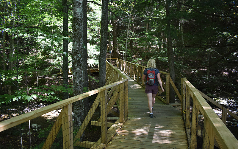Mad River Path Board Member Dori Ross walking across the bridge next to the McCollough Barn into the Chase Brook Town Forest. 