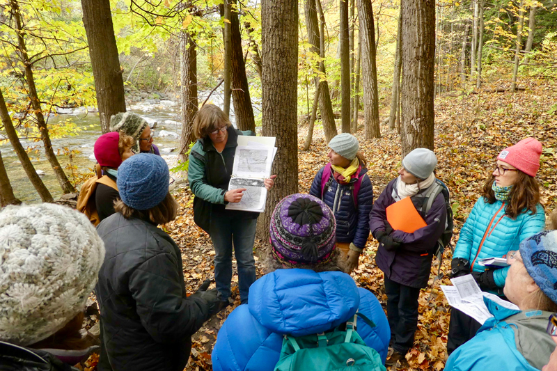 Kristen Underwood, a hydrogeologist with South Mountain Research and Consulting Services, helps Vermont Master Naturalist Bristol Five-Town Area Program participants uncover the story of an old coffin factory along the New Haven River that burned down in 1947 by exploring the foundations. Photo by Monica Przyperhart.