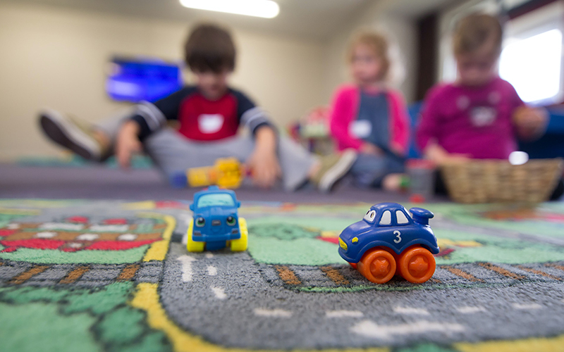 Kids playing with toy cars on a mat.