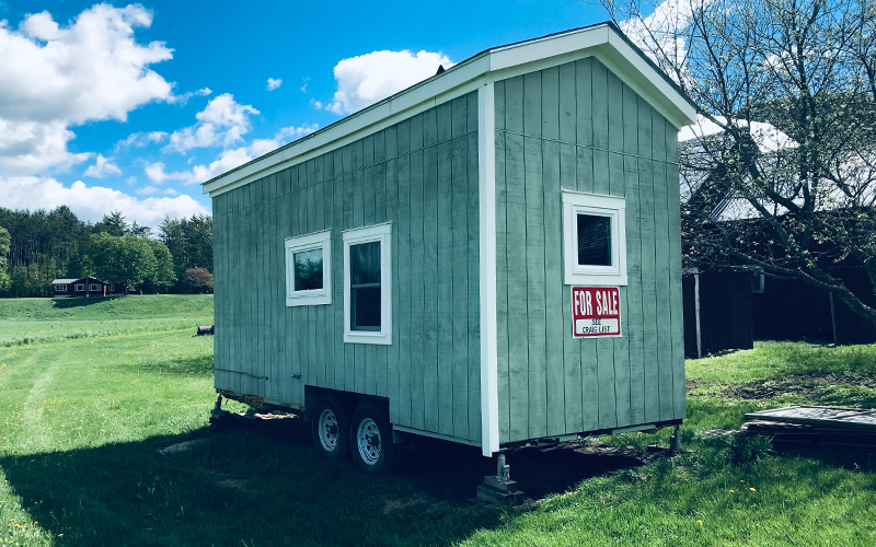 A tiny house on a trailer with a for sale sign on the side.