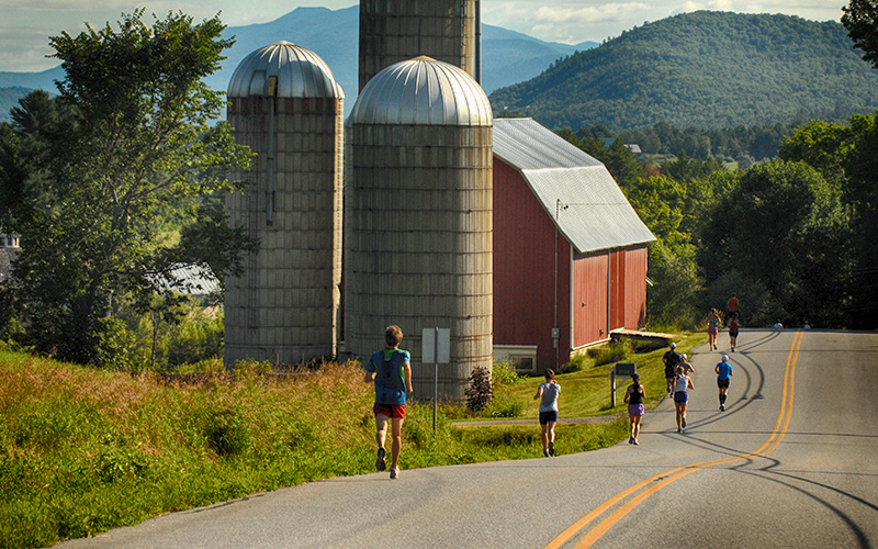 Mad Marathon runners on a mountain road passing a barn and silos.