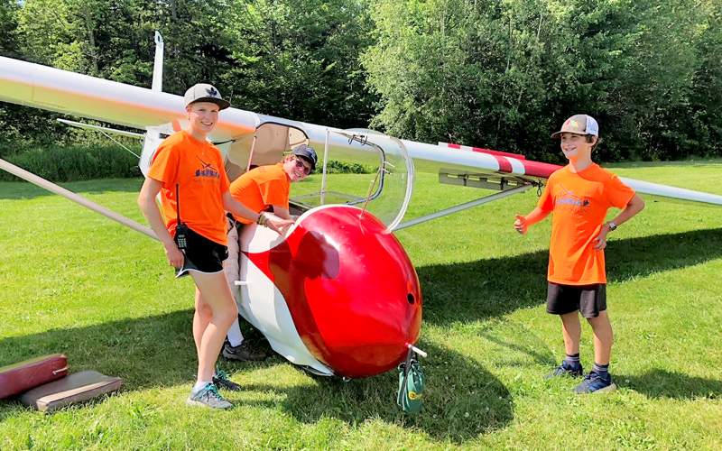 Boys standing around a glider. Silas Gulley (right) after his first flight, with fellow line crew members Maia Pasco (left) and Tim Wilson (center).