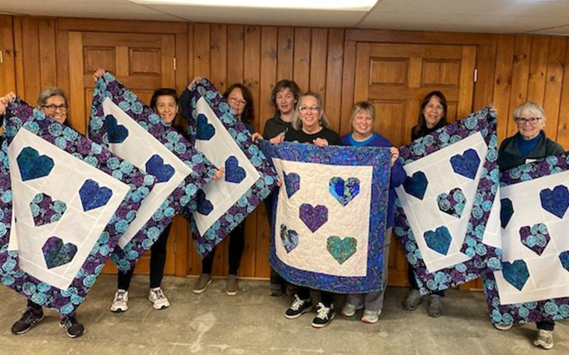 Local quilters display their creations. Left to right: Tisa Rennau, Lee-Anne Martin, Sally Boudreau, Cory Stephenson (librarian), Jeb Bouchard, Lisa Therrien, Carla Lewis, and Dotty Kyle.