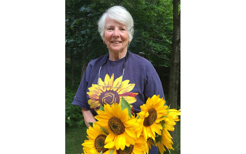 Dotty Kyle in a sunflower shirt with a bunch of sunflowers.