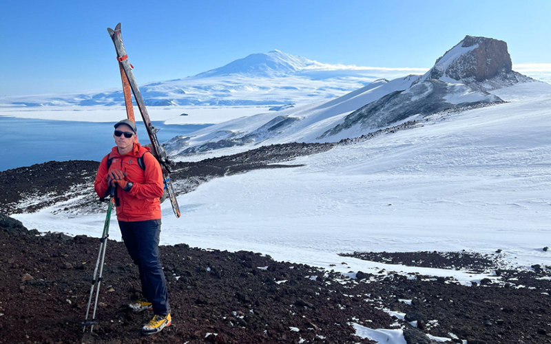 Tim Farr with skis on his back hiking mountains in Antarctica.