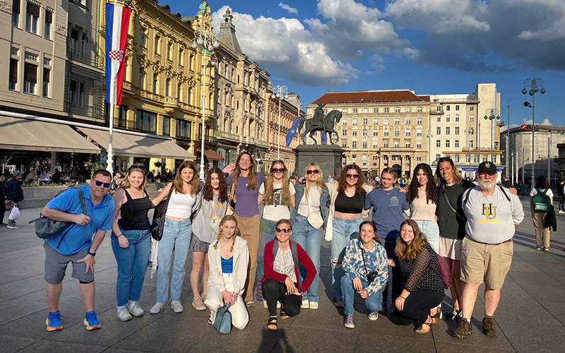 The Harwood girls’ basketball team, coaches and two people from PH International pose for a photo in the town square in Zagreb, Croatia. Coaches: Bethany Fuller, Greg Titus, and Tommy Young. Players: Cammie Rocheleau, Abby Young, Cierra McKay, Ciera Fiaschetti, Jill Rundle, Mia Lapointe, Sadie Nordle, Quinn Nelson, Eloise Lilley, Addy Olney, Roanha Chalmers. PH International: Tracy Guion and Emily Wilmers.